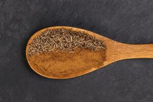 Cumin spice whole powder wooden spoon on black slate background photo