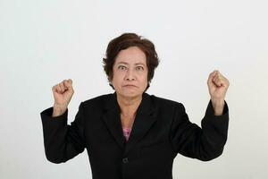 Elderly asian Chinese female on white background wearing black suit point at camera angry furious fist in air photo