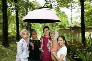 group of woman friends Malay Chinese Indian Asian outdoor park lake nature walking under one umbrella secure safe rain photo