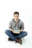 Middle eastern Caucasian young in casual dress sit on floor holding heavy books annoyed surprised expression on white background photo