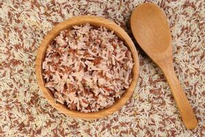 Cooked and raw mixed low glycaemic index healthy rice grain basmati millet buckwheat red rice in wooden bowl spoon bed of rice over white background photo