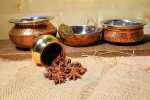 Aromatic spice Star anise pouring from small brass copper pot jute textile wooden background photo