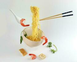 Yellow seafood prawn coriander leaf noodle soup elevated flying suspended in air with soup spoon and chopstick prawn coriander leaf tofu on white background photo