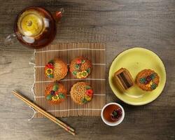 Colourful flower decorated mooncake Chinese mid autumn festival on bamboo food mat background slice cut piece layered on yellow ceramic plate glass teapot teacup chopsticks photo