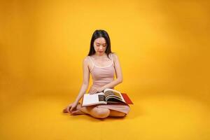 Beautiful young south east Asian woman sit down on floor yellow orange color background read study book magazine pose fashion style elegant beauty mood photo
