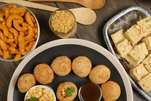 verity of indian bengali street food tea time snacks onion pakoda crunchy spicy lentils moong dal fry sweet shompapri chaat pani puri fuska on rustic retro table plate brass copper pots silver tray photo