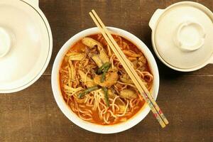 Malaysian curry yellow mee noodle with roasted chicken slice in white bowl chopstick on rustic wooden background photo