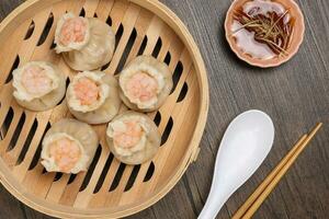 Prawn shrimp shaomai dim sum dumpling in bamboo steamer sauce chopsticks soup soon on rustic wood background photo