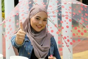 Young Asian Malay muslim woman headscarf outdoor green pose with umbrella thumbs up finger sing photo