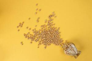 Soyabeans pouring from hart shape glass bottle on yellow background photo