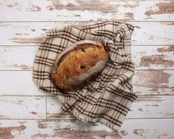 Rustic whole grain artisan bread loaf with cranberry raisin dry fruit nuts wrapped in checkers cloth with wooden table top flat lay view photo