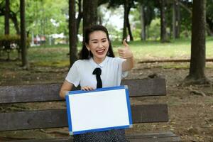 joven asiático chino mujer al aire libre parque instalaciones libro archivo carpeta ordenador portátil computadora teléfono sentar estar estudiar mezclarse foto