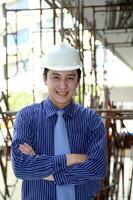 South East Asian young Malay Chinese man wearing white yellow safety helmet tie look at camera smile cross hand photo