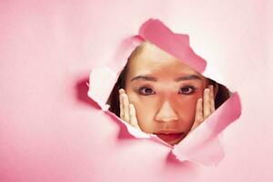 Young beautiful Asian woman expression through torn paper hole photo