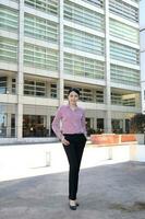 Young south east Asian middle woman business colleague in front of a tall building look forward at camera photo