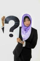 South East Asian young Malay woman wearing formal business office ware headscarf on white background holding question mark sign photo