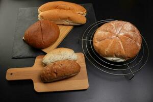 Freshly baked bread loaf bun roll round long mix verity on wooden board metal grill over black background photo