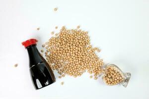 Soyabeans pouring from hart shape glass bottle around bottle of soya bean sauce on white background photo