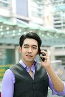 Southeast Asian young office business man wearing vest talk on phone thinking happy expression outdoor premises photo