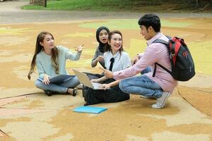 Young asian malay chinese man woman outdoor park sit on ground study talk discuss point laptop file book backpack mingle fun meet photo