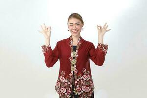 Asian woman traditional red maroon kebaya sharong on white background posing finger circle ok sign photo