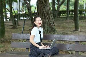 joven asiático chino mujer al aire libre parque instalaciones libro archivo carpeta ordenador portátil computadora teléfono sentar estar estudiar mezclarse foto