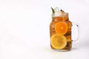 Liquid ice lemon orange tea with slice green leaf cinnamon stick in transparent glass jar mug on white background photo