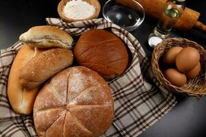 recién horneado un pan pan bollo rodar redondo largo mezcla verdad envuelto en a cuadros cocina tela servilleta toalla trigo flor petróleo agua sal huevos laminación alfiler pizarra Roca terminado negro antecedentes foto