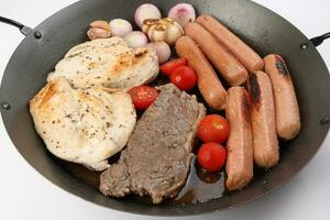 Mix meet pan chicken breast beef steak sausage tomato onion garlic oil fry grill on metal frying pan two wooden handle on white background photo