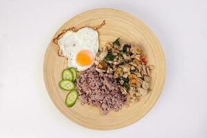 Thai fusion stair fried chicken with Thai basil and cashew nut with health brown rice fried egg sauce cucumber on woody plate over white background photo