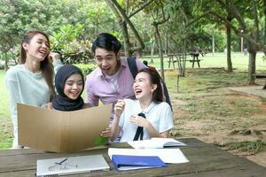 Young asian malay chinese man woman outdoor on park bench table study talk discuss point laptop file book photo