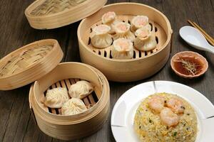 Prawn shrimp shaomai Xiao long bao dim sum dumpling chicken prawn fish seafood vegetable in bamboo steamer fried rice on plate sauce chopsticks soup spoon over rustic background photo