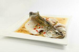 Thai style steam sea bass barramundi with lemon garlic chilli clear sauce on white serving dish photo