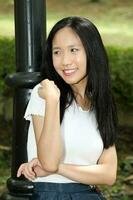 One Asian Chinese  woman posing smile look forward towards camera confident outdoor green park photo