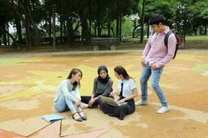 joven asiático malayo chino hombre mujer al aire libre parque libro archivo carpeta ordenador portátil computadora teléfono sentar estar estudiar mezclarse foto