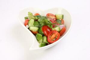 Indian Subcontinent style tomato cucumber onion chili coriander salad in hart shape white dish on white background photo