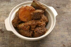 Asian style Beef bhuna dry curry with potato in ceramic bowl over rustic wooden background photo
