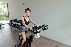 Beautiful attractive middle age southeast Asian woman exercising stationary bicycle cycle bike in a gymnasium healthy lifestyle look forward smile at camera photo