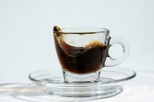 Coffee splash wave in transparent glass espresso cup saucer full of liquid coffee on white background photo