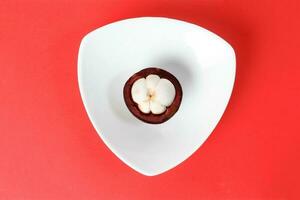 Purple mangosteen fruit pealed half on white hart shape plate red background photo