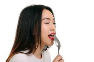 Beautiful young south east Asian woman pretend acting posing holding empty spoon in hand on lips tongue eat taste lick white background eye close imagine yummy photo