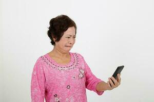 Elderly asian Chinese female on white background read text massage on phone serous lips bent disgusted worried photo