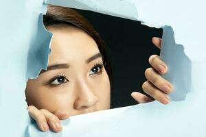 Young beautiful Asian woman expression through torn paper hole photo