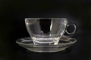 Empty transparent glass see through coffee tea cup saucer on black background photo