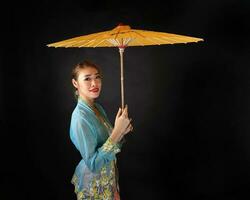 Asian woman in tractional kebaya carrying umbrella on black background photo