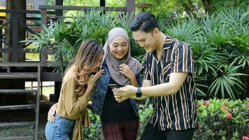 Young Asian Malay man woman outdoor green park talk discuss hand phone text massage photo