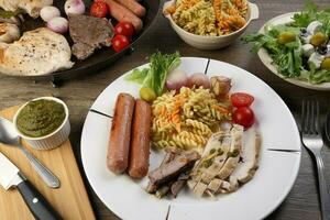Mix meet chicken beef steak sausage tomato onion garlic fry grill metal pan colorful pasta green salad cheese olive mint basil pesto sauce board knife fork spoon sliced served plate wooden table photo