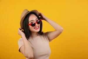 Beautiful young south east Asian woman red frame sunglass hat pose style fashion peak happy on yellow orange background hand behind head pull photo