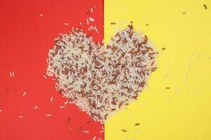 Mixed low glycaemic index healthy rice grain basmati millet buckwheat red rice hart shape on red yellow background photo