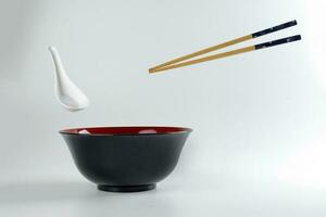 Empty oriental Japanese Chinese soup bowl spoon chopstick elevated flying in air red black white photo